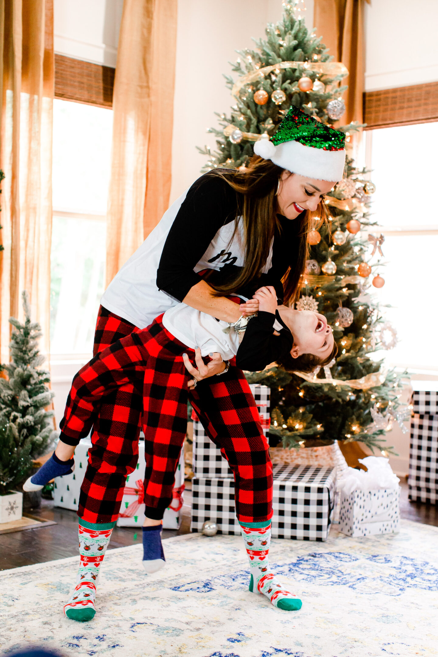 Heather tickles her son in front of a Christmas tree as they both laugh 