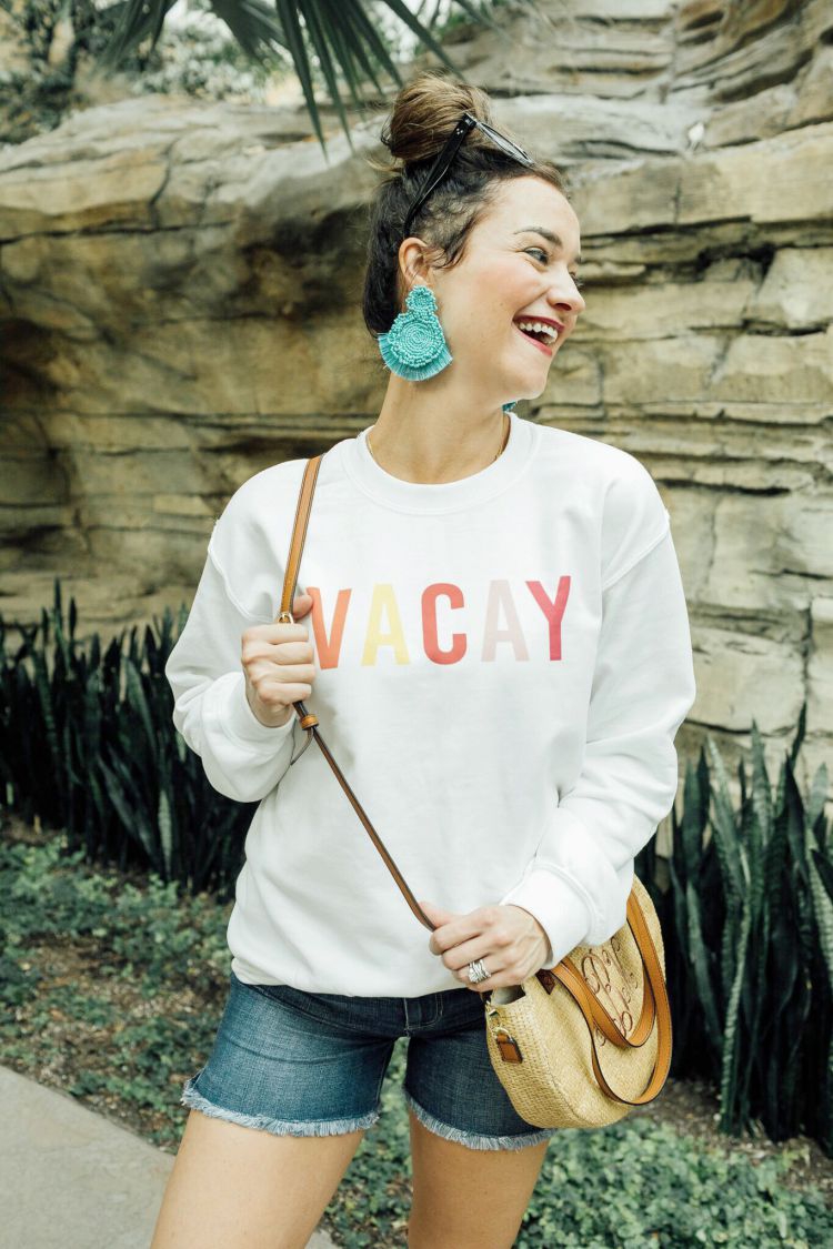 A Complete Dallas Travel Guide featured by top US travel blog, My Life Well Loved: image of a woman in Dallas wearing a Pink Lilly sweatshirt, Liverpool denim shorts, Marleylilly crossbody bag , Accessory Concierge statement earrings, zeroUV square sunglasses and Comfortiva sandals