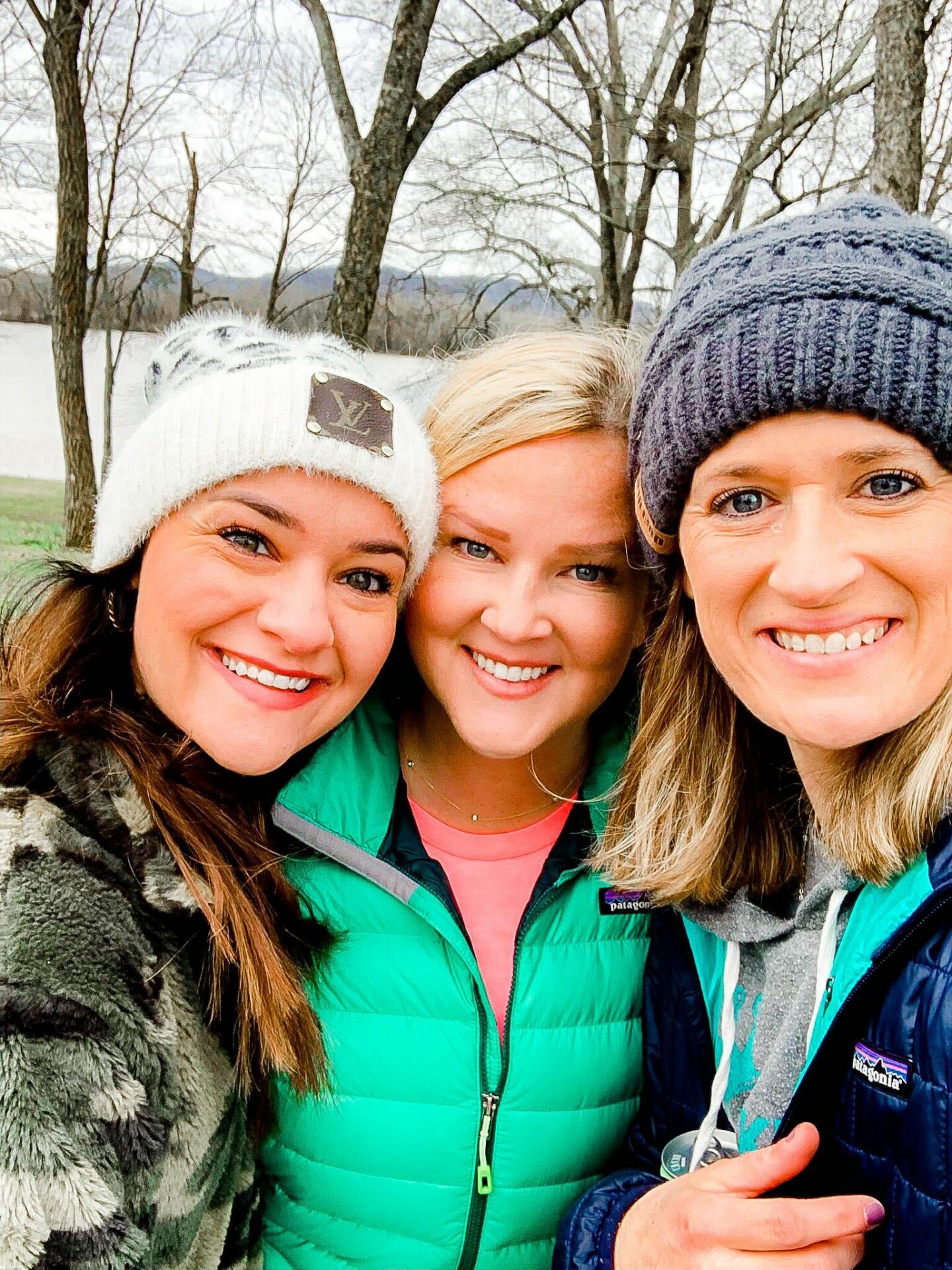 Heather and two of her friends stand close together and smile at the camera. They are all wearing beanie hats. 