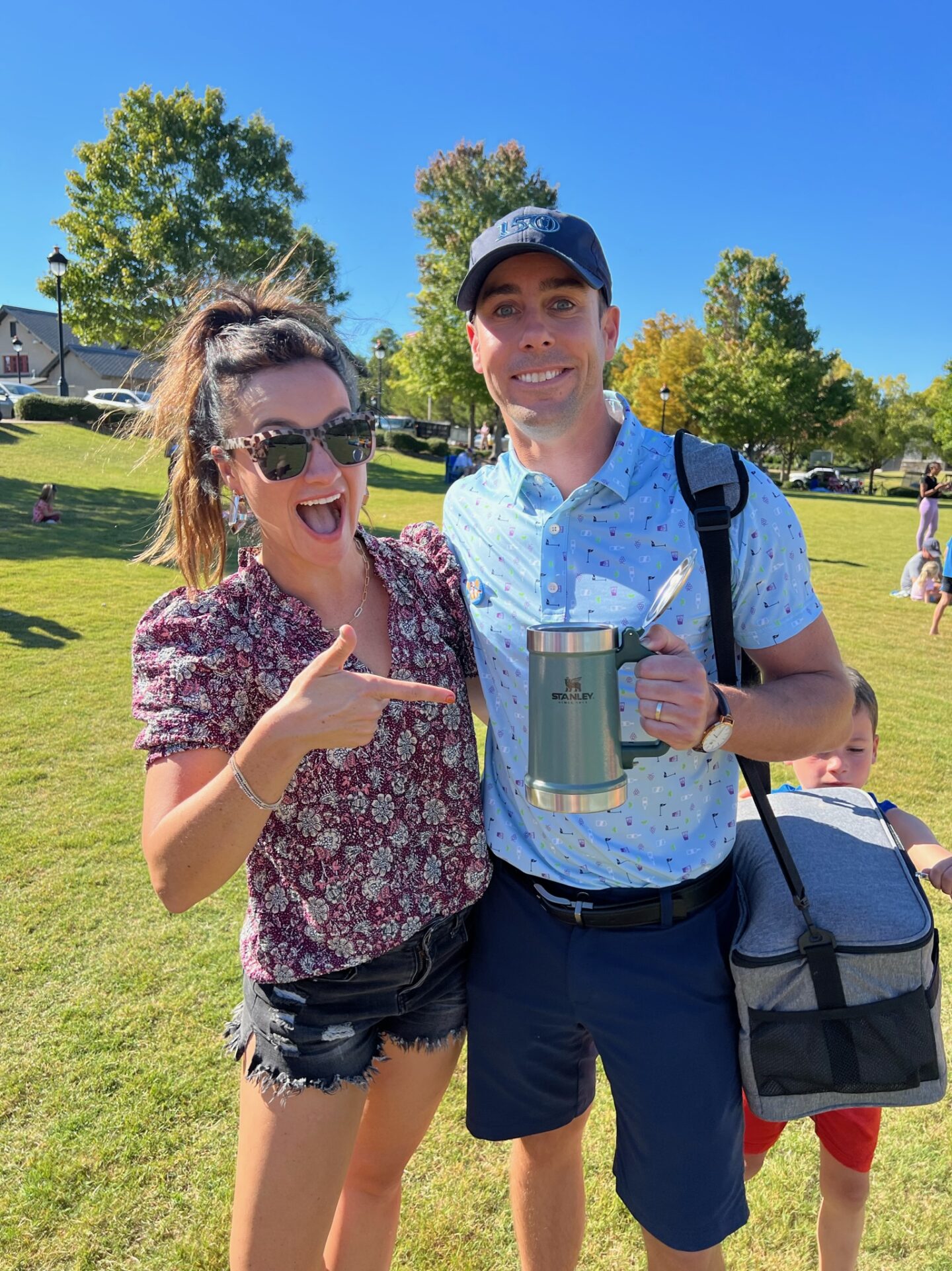 Heather and Eric smile together on the golf course holding a Stanley cup