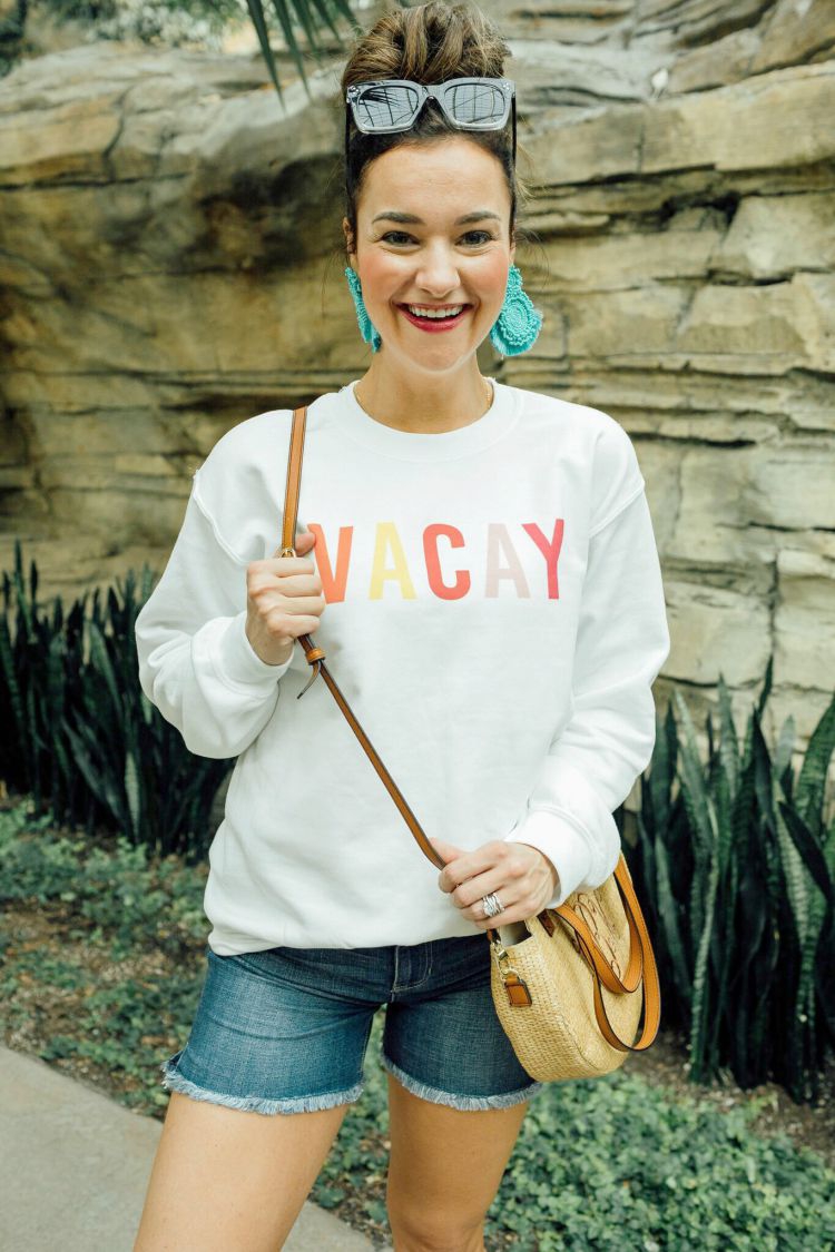 A Complete Dallas Travel Guide featured by top US travel blog, My Life Well Loved: image of a woman in Dallas wearing a Pink Lilly sweatshirt, Liverpool denim shorts, Marleylilly crossbody bag , Accessory Concierge statement earrings, zeroUV square sunglasses and Comfortiva sandals